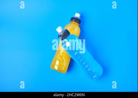 Flaches isotonisches Energy-Orange-Gelb und blaues Sportgetränk in Plastikflaschen auf blauem Hintergrund. Ermöglicht die Aufrechterhaltung des optimalen Wassergleichgewichts Stockfoto