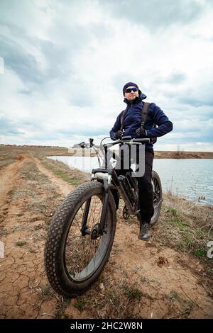 Ein Mann auf einem fetten Fahrrad in der Nähe des Sees. Ein sportlicher Lifestyle. Stockfoto