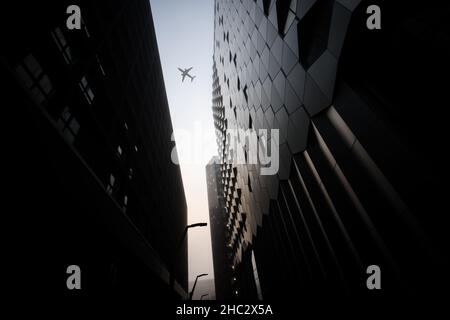 Flugzeug Jumbo Jet Passagierflugzeug fliegen zwischen modernen Stadtzentrum Wolkenkratzer an nebligen nebligen Tag dramatische Beleuchtung und Stahlgebäude futuristisch Stockfoto