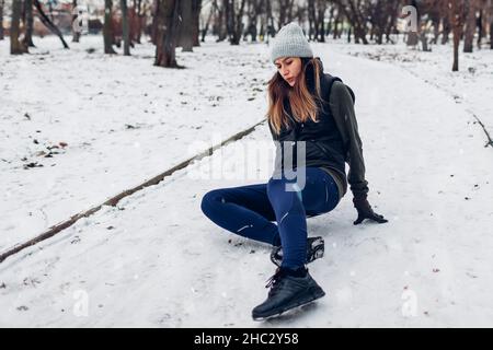 Die Läuferin fiel während des Trainings im verschneiten Winterpark nieder. Frau fühlt Schmerzen auf dem Boden liegen. Sicherheit beim Training Stockfoto