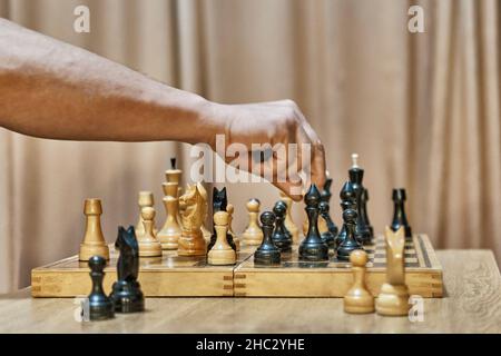 Alte Schachfiguren aus Holz auf Schachbrett. Hand eines erwachsenen Mannes, der sich mit weißem Bauer bewegt Stockfoto