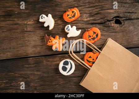 Helle Halloween Tischdekoration mit weißen und orangen Ingwer-Keksen auf einem braunen Holztisch. Kürbis und Geister. Stockfoto