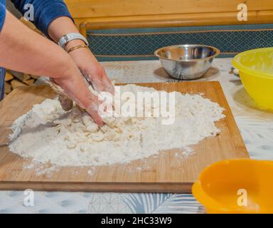 Nahaufnahme von Frauenhänden, die Mehl und Eier auf einem hölzernen Gebäckbrett kneten Stockfoto