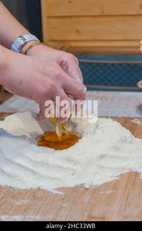 Nahaufnahme von Frauenhänden, die Mehl und Eier auf einem hölzernen Gebäckbrett kneten Stockfoto