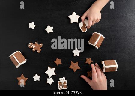 Kinder bereiten sich auf Weihnachten vor. Zuckerglasierte Lebkuchenkekse in den Händen von Kindern. Schwarzer Hintergrund. Stockfoto