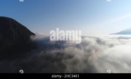 Schöner Sonnenaufgang über den Wolken, Blick von der Spitze des Berges. Antenne für langsame Bewegung von dicken Wolken gegen den blauen klaren Himmel und die helle Sonne. Stockfoto