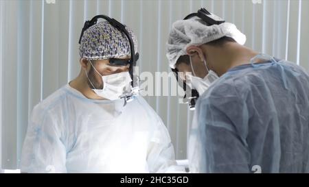Chirurgen tragen eine spezielle Brille während der Operation im Krankenhaus. Arzt und Assistent arbeiten im Operationssaal, Konzept der professionellen Ausrüstung Stockfoto