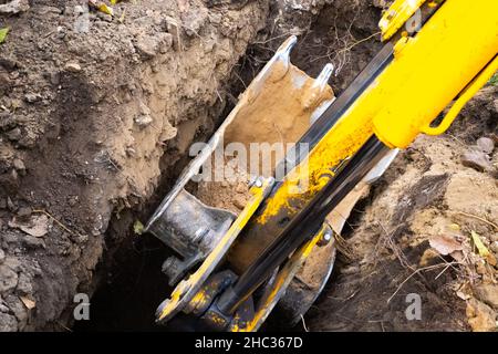 Der Baggereimer gräbt ein tiefes Loch. Erdarbeiten für die Installation von Rohrleitungen und Klärgruben. Stockfoto