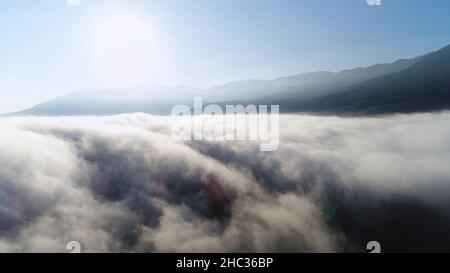 Schöner Sonnenaufgang über den Wolken, Blick von der Spitze des Berges. Antenne für langsame Bewegung von dicken Wolken gegen den blauen klaren Himmel und die helle Sonne. Stockfoto