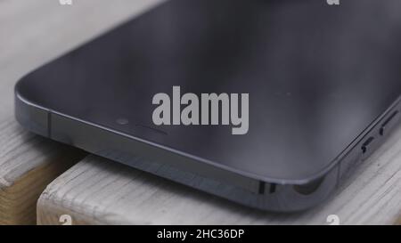 Nahaufnahme eines Teils eines schwarzen Bildschirms eines neuen Smartphones auf Holzbank Hintergrund. Ein neues ausgeschaltetem Gerät wird auf einem Prüfstand belassen. Stockfoto