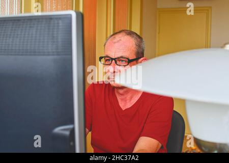 Im mittleren Alter Mann mit Brille am Schreibtisch sitzen. Reifer Mann mit Personal Computer. Senior Concept Stockfoto