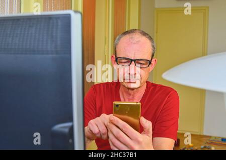 Mann mittleren Alters mit Brille am Schreibtisch. Reifer Mann mit Mobiltelefon. Senior-Konzept. Mann im Heimbüro. Stockfoto