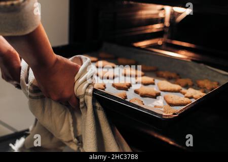 Nahaufnahme einer Frau, die ein Backblech mit weihnachtsplätzchen aus dem Ofen nimmt Stockfoto