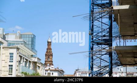 Seitenansicht eines neuen mehrstöckigen Gebäudes im Bau. Der Kontrast zwischen modernem Gebäude und alter schöner Kirche oder Tempel. Stockfoto