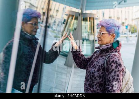 Italien, modische ältere Frau berührt Glasoberfläche in der Stadt Stockfoto