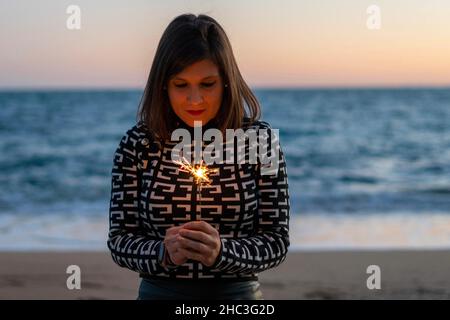 Junge Frau, die mit ihrem magischen Funkeln im Sand einen Wunsch macht Stockfoto