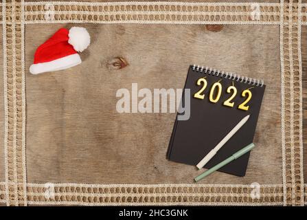 2022 Kerzennummern eines nächsten Ohres auf schwarzem Notizbuch und kleinem Weihnachtsmann-Hut, Holzhintergrund, mit leerem Platz für Text. Stockfoto