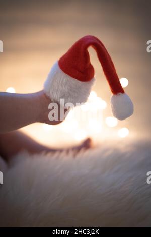 Füße eines Neugeborenen mit einem Weihnachtsmann-Hut auf einer flauschigen Decke mit Weihnachtslichtern im Hintergrund Stockfoto