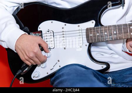 Nahaufnahme eines jungen Mannes, der die Lautstärke der E-Gitarre anpasst. Musik, Instrumentenausbildung, Unterhaltung, Rockstar, Musikkonzert und Lernkonzept Stockfoto