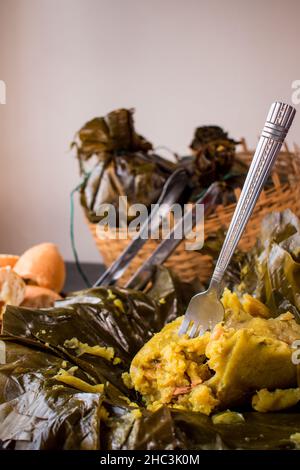 Traditionelles kolumbianisches Essen, bekannt als „Tamal“, verpackt mit Blättern in einem Korb auf einem schwarzen Tisch Stockfoto