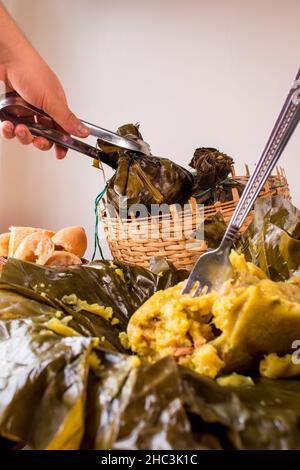 Nehmen Sie ein traditionelles kolumbianisches Essen, das als „Tamal“ bekannt ist und mit Blättern aus einem Korb auf einem schwarzen Tisch verpackt ist Stockfoto