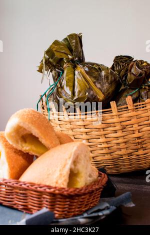 Traditionelles kolumbianisches Essen, bekannt als „Tamal“, verpackt mit Blättern in einem Korb auf einem schwarzen Tisch Stockfoto