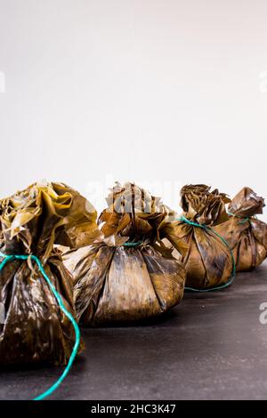 Traditionelles kolumbianisches Essen, bekannt als „Tamal“, eingewickelt mit Blättern auf einem schwarzen Tisch Stockfoto