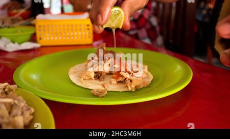 mexikanischer Mann, der Limettensaft auf seine traditionellen Carnitas-Tacos aus Michocan setzte. Hochwertige Fotos Stockfoto