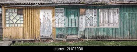 Alte verlassene grüne Holzhausfassade mit vielen Türen und Fenstern. Panoramablick. Stockfoto