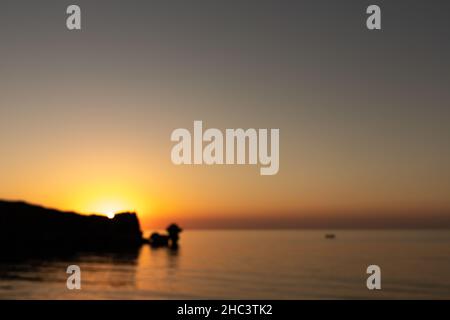 Sonnenuntergang auf dem Meer, Felsen und Sonne, Silhouette und Boot mit Fischern. Unscharfer Hintergrund. Asowschen Meer, Russland. Stockfoto