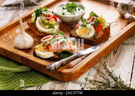 Appetitliche Canapes oder Sandwiches mit geräuchertem Lachs. Toast mit Fisch, Weichkäse, Eiern, Zwiebelringen und Salat. Leckeres Frühstück oder Snack Stockfoto