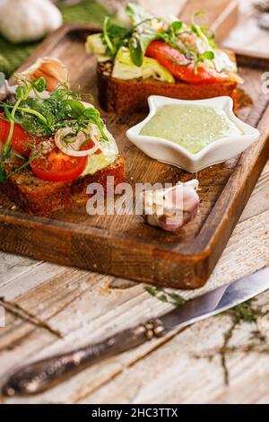 Appetitliches Mittagessen oder Snack. Kanapees oder Sandwiches mit geräuchertem Lachs. Toast mit Fisch, Weichkäse, Eiern, Zwiebelringen und frischem Salat. Knoblauchsoße Stockfoto