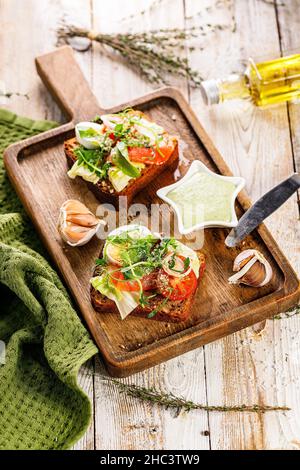 Appetitliche Canapes oder Sandwiches mit geräuchertem Lachs. Toast mit gesalzenem Fisch, Käse, Ei, Zwiebelringen und Salat. Knoblauchsauce mit Käse und Kräutern Stockfoto