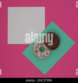 Zwei Donuts, die mit Schokoladenbröseln auf einer hellgrünen Oberfläche mit weißem Kopierraum bestreut wurden, alle auf einem rosa Hintergrund. Minimale Flachfleckenszene. Stockfoto