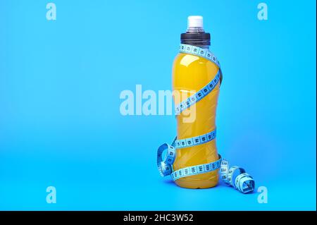 Isotonische Energie orange gelb Sportgetränk in Plastikflasche und messen Klebeband um sie auf blauem Hintergrund. Ermöglicht die Aufrechterhaltung des optimalen Gleichgewichts von Wasser, Salz und Elektrolyten Stockfoto