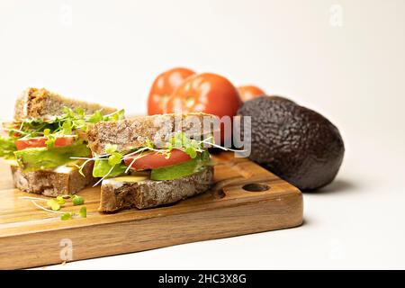 Nahaufnahme eines Sandwiches mit glutenfreiem Brot, Tomate, Avocado, veganem Käse und Microgreens Stockfoto