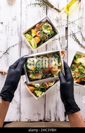 Hände in schwarzen Handschuhen packen ein Business Lunch in einen Karton. Konzept Food Delivery Service. Restaurant zum Mitnehmen. Leckeres Essen bei der Arbeit Stockfoto