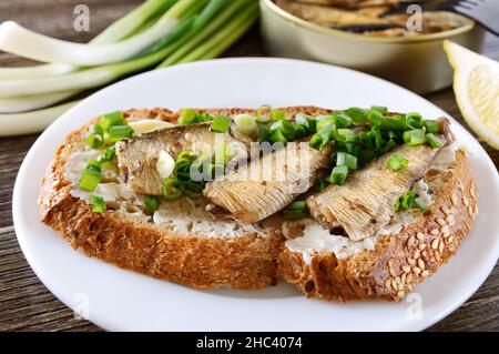 Fischsandwich mit Sprotten, Butter und grünen Zwiebeln auf weißem Teller, Nahaufnahme Stockfoto