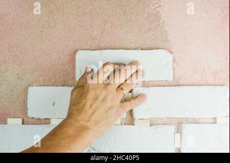 Die Hand des Meisters legt dekorative Fliesen unter den Ziegel an die Wand. Das Ende der modernen Veredelungsarbeiten Stockfoto