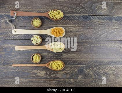 Holzlöffel und Holzschüsseln mit trockener italienischer Pasta in verschiedenen Formen auf einem rustikalen braunen Tisch. Draufsicht Stockfoto