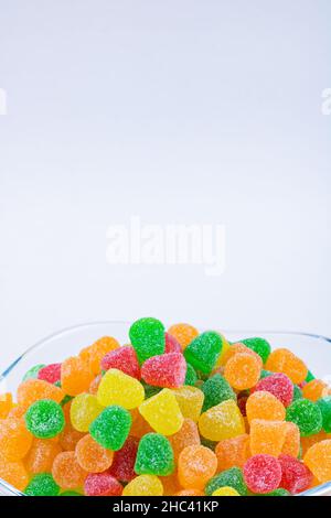 Leckere Süßigkeiten. Gummy Bonbons in der Schüssel isoliert auf weißem Hintergrund. Vertikales Textfoto. Stockfoto