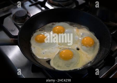 Vier Eier werden in einer schwarzen Pfanne auf dem Gasherd gebraten Stockfoto