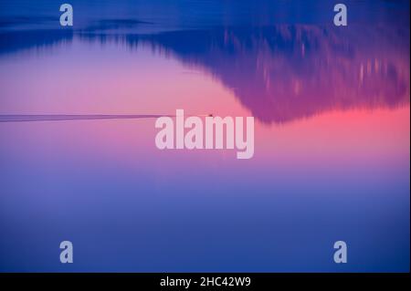 Faszinierende Landschaft, die sich in einem See mit einem Boot bei Sonnenuntergang widerspiegelt Stockfoto