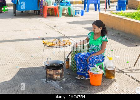 Eine burmesische Frau mit Thanakha im Gesicht kocht und frittiert Straßenessen, um sie zu verkaufen, in Yangon, Burma Stockfoto