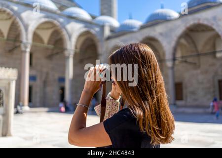 Braunhaarige Touristenfrau, die an einem sonnigen Tag in İstanbul die Suleymaniye-Moschee fotografiert. Reisen und aktiver Lifestyle, Sommerurlaubskonzept. Stockfoto