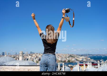 Rückansicht einer Fotografin, die die Arme nach oben zum blauen Himmel hebt, und Istanbul City View. Stockfoto