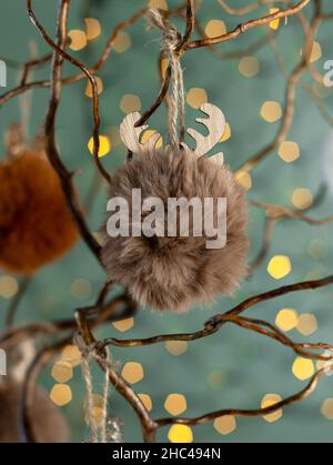 Alternativer Zweig Baum ist mit flauschigen Kunstpelzkugeln in neutralen Brauntönen dekoriert. Modernes und elegantes nordisches Weihnachtsdekor. Stockfoto