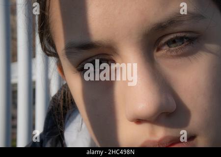 In einer extremen Nahaufnahme eines Teenagers, das zärtlich auf die Kamera starrte, wurde ein menschliches Gesicht zugeschnitten. Sonnenlicht erhellt ihr Gesicht, ihre Augen sind grün. Stockfoto