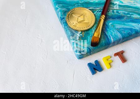 Nicht-fungible Token-Konzept. NFT Wort neben Ethereum Krypto Münze und Pinsel auf Leinwand mit Malerei auf weißem Hintergrund mit Kopierraum für Text. Stockfoto