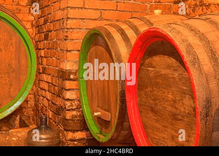 Weinfässer im alten Keller des Weinguts gestapelt. Fässer Wein in einem Weinkeller, einem alten Weinkeller mit gewölbten Ziegeldecken Stockfoto